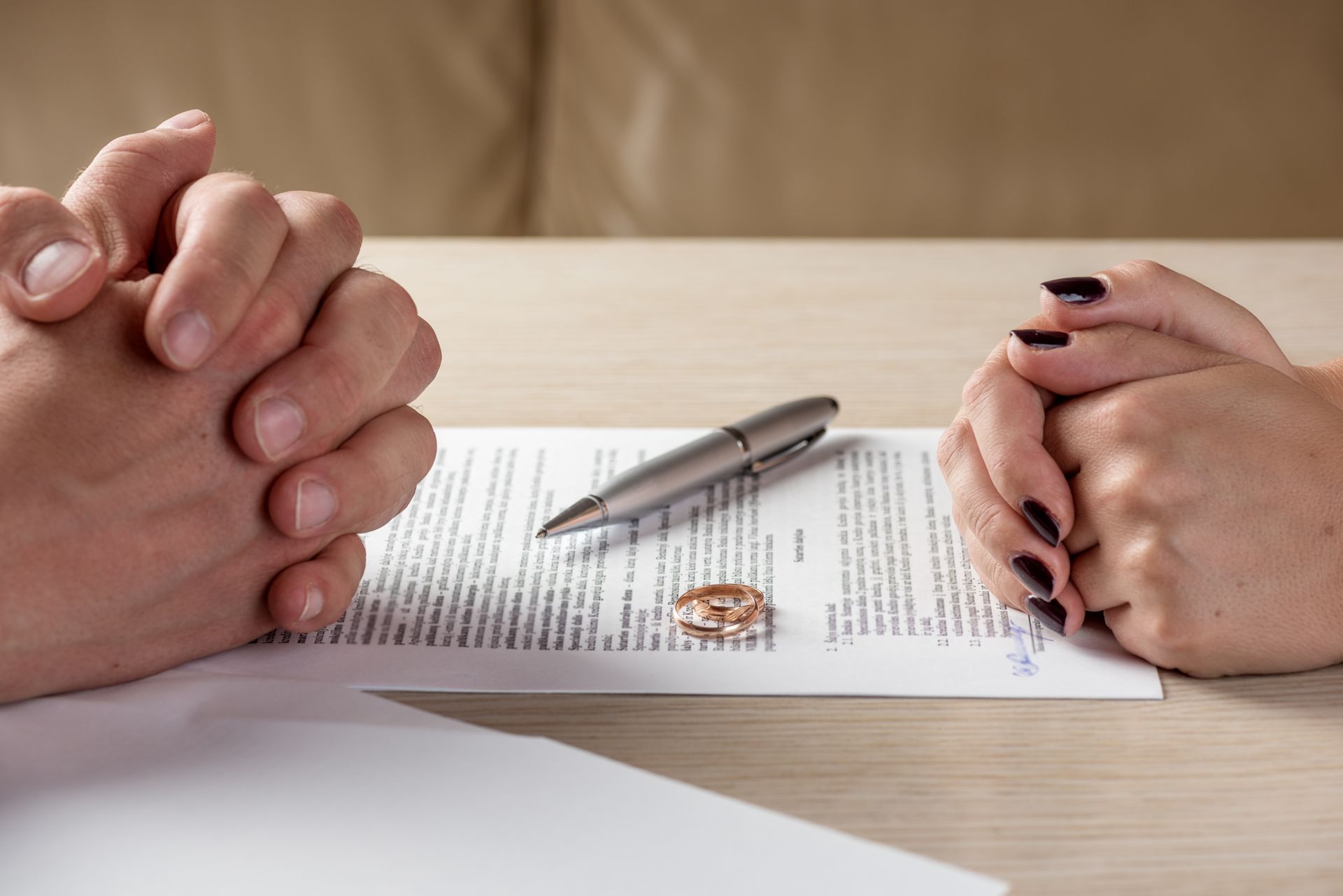 Deux mains jointes sur un contrat, un stylo et une alliance brisée posés sur un bureau.