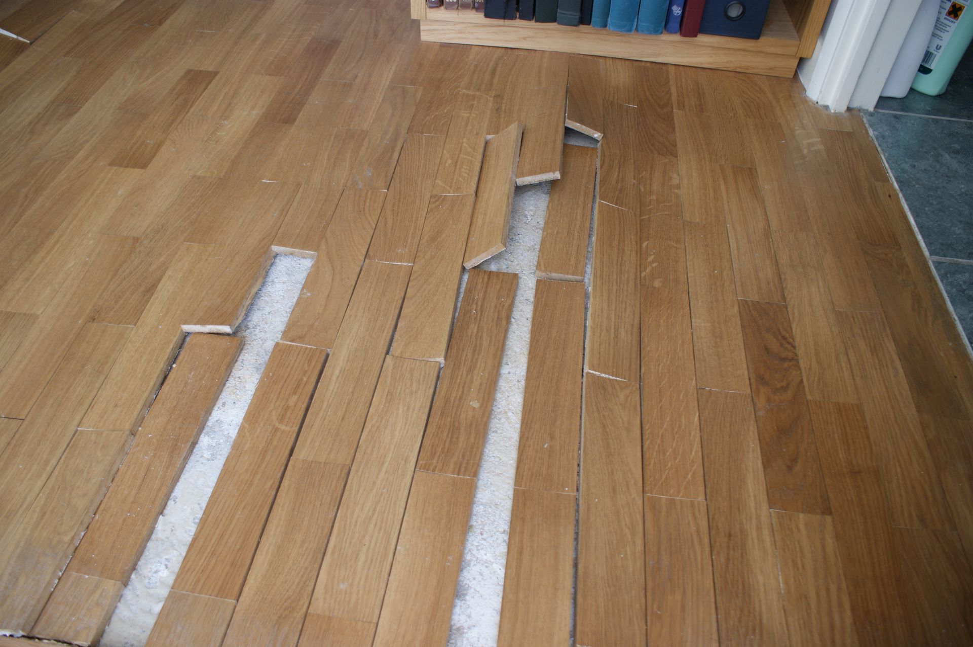 Plancher en bois avec des lattes soulevées et manquantes, sous-couche apparente.
