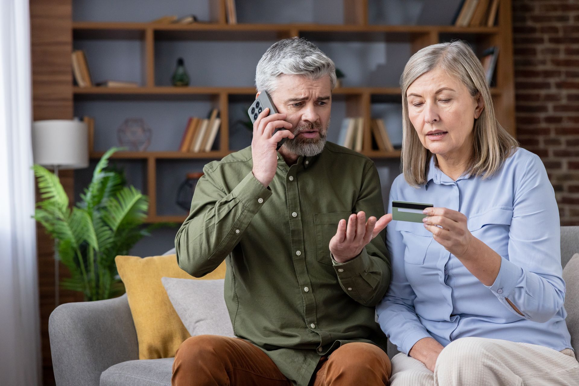 Deux personnes sont assises sur un canapé, en train d'observer une carte bancaire, tandis que l'une d'elles parle au téléphone.