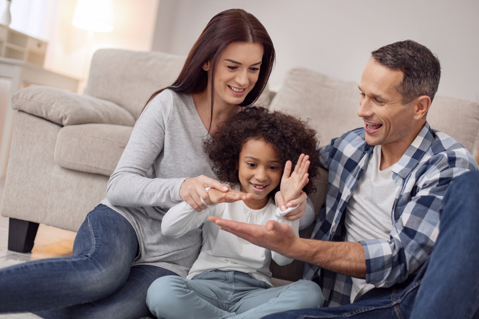 Une famille assise sur un canapé, souriante et jouant ensemble avec un enfant au centre.