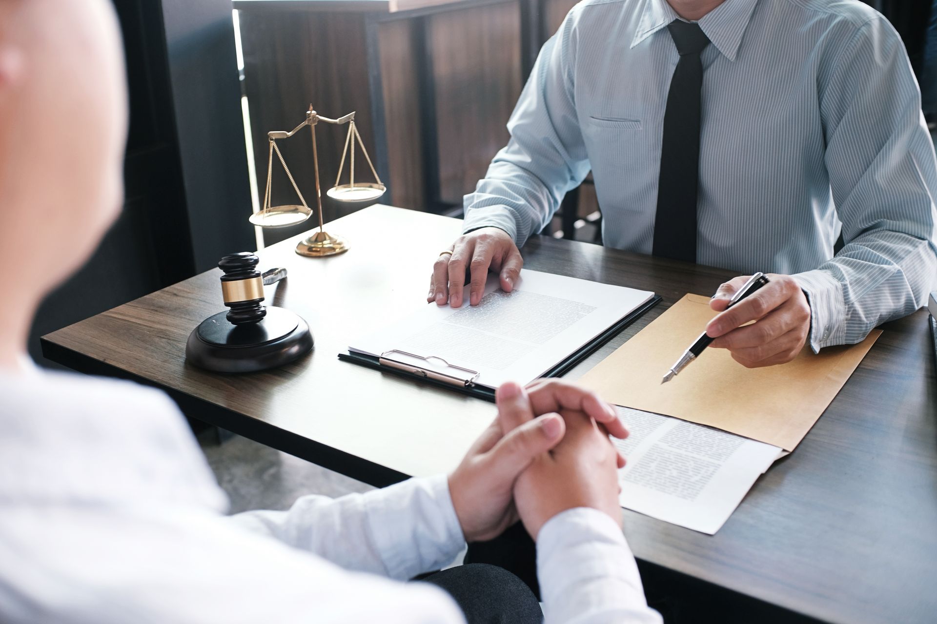 Deux personnes assises à un bureau avec des documents, une balance de justice et un stylo.