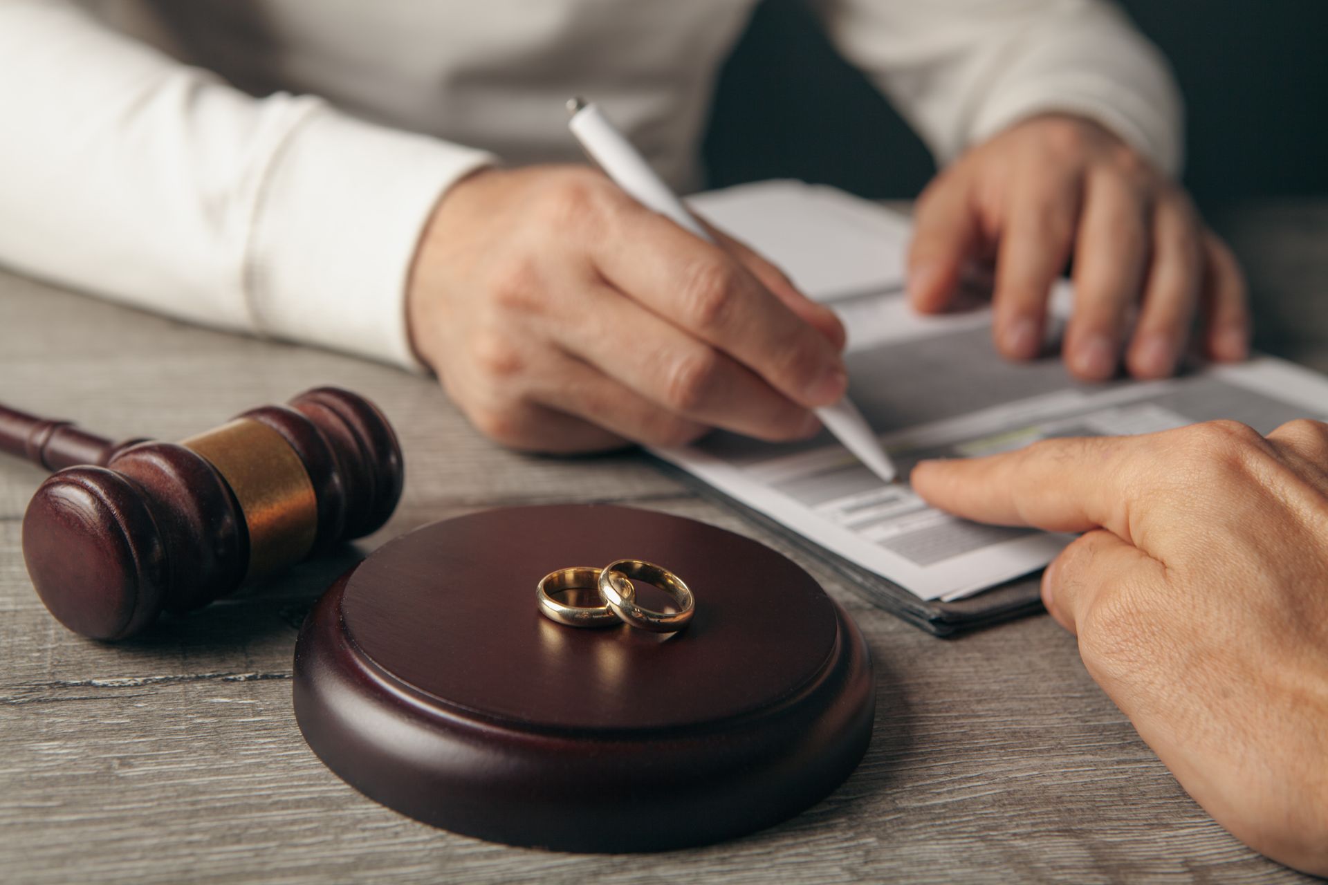 Alliances sur un socle en bois tandis qu'une personne signe un document à côté d'un maillet.