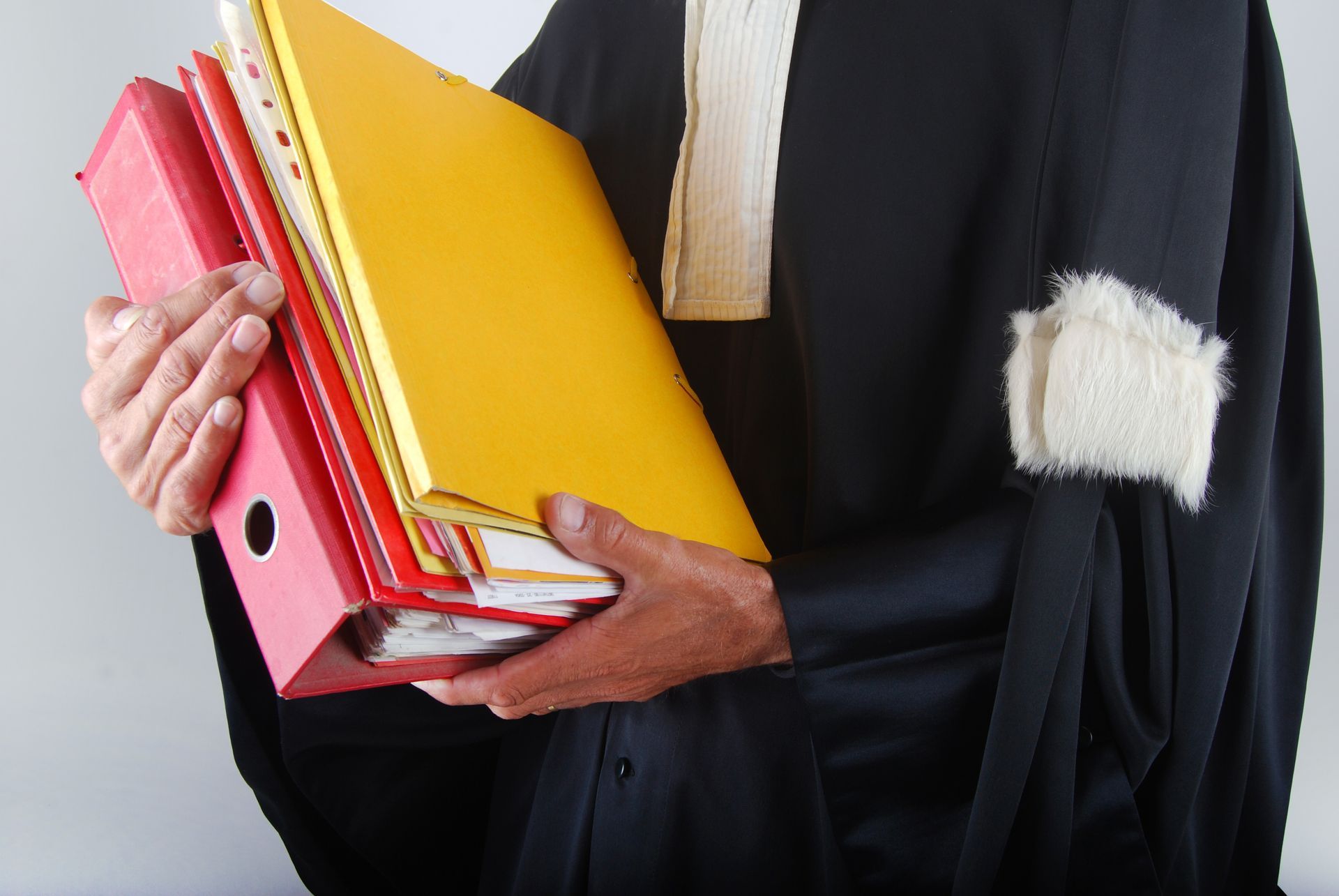 Une personne en robe d'avocat tenant des dossiers rouges et jaunes.