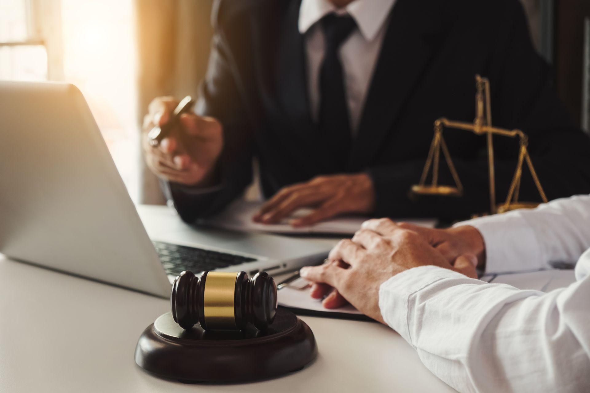 Maillet, balance de justice, ordinateur portable posé sur un bureau avec un homme en costume noir en arrière-plan.