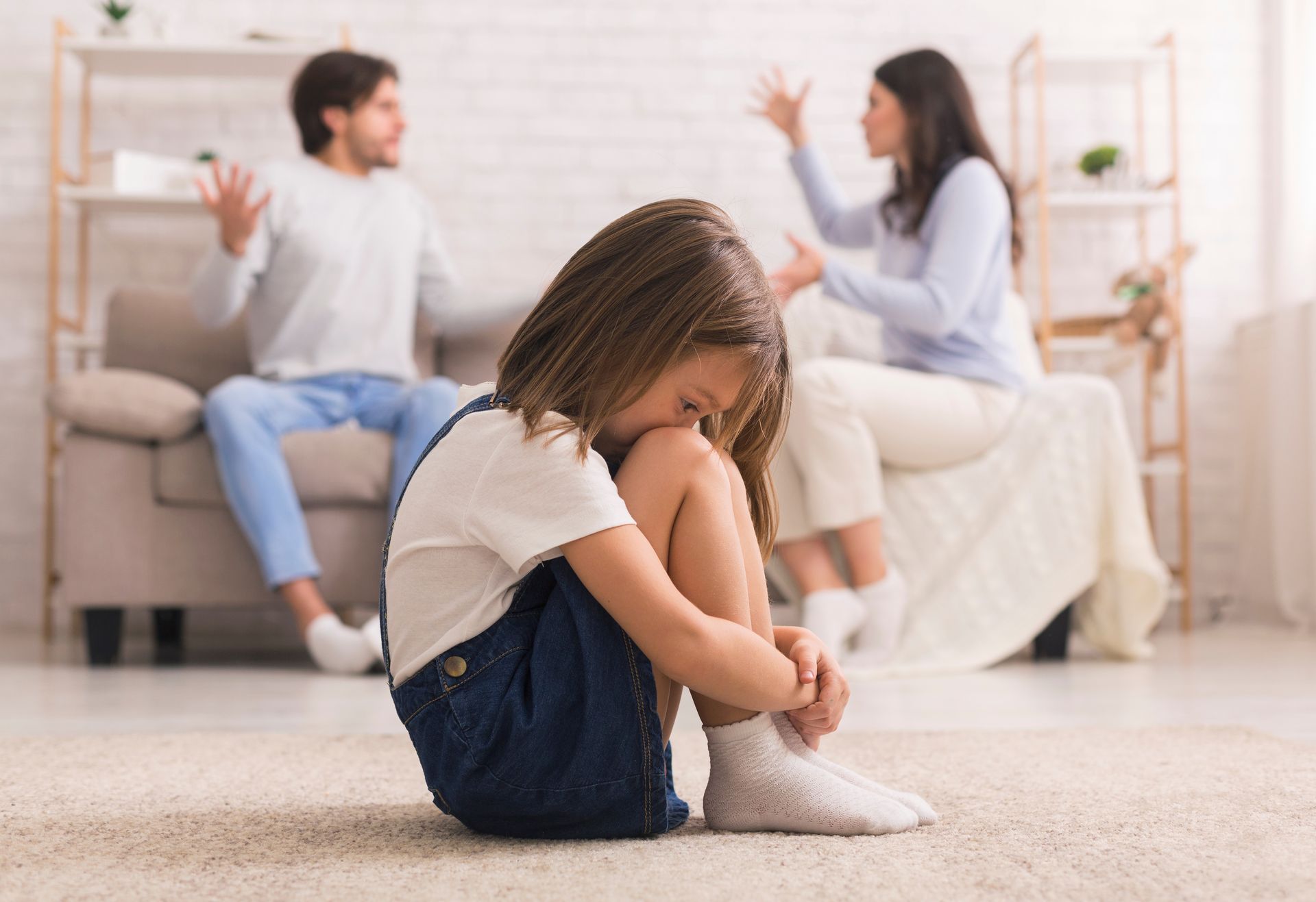 Un enfant assis par terre pendant que ses parents se disputent en arrière-plan.