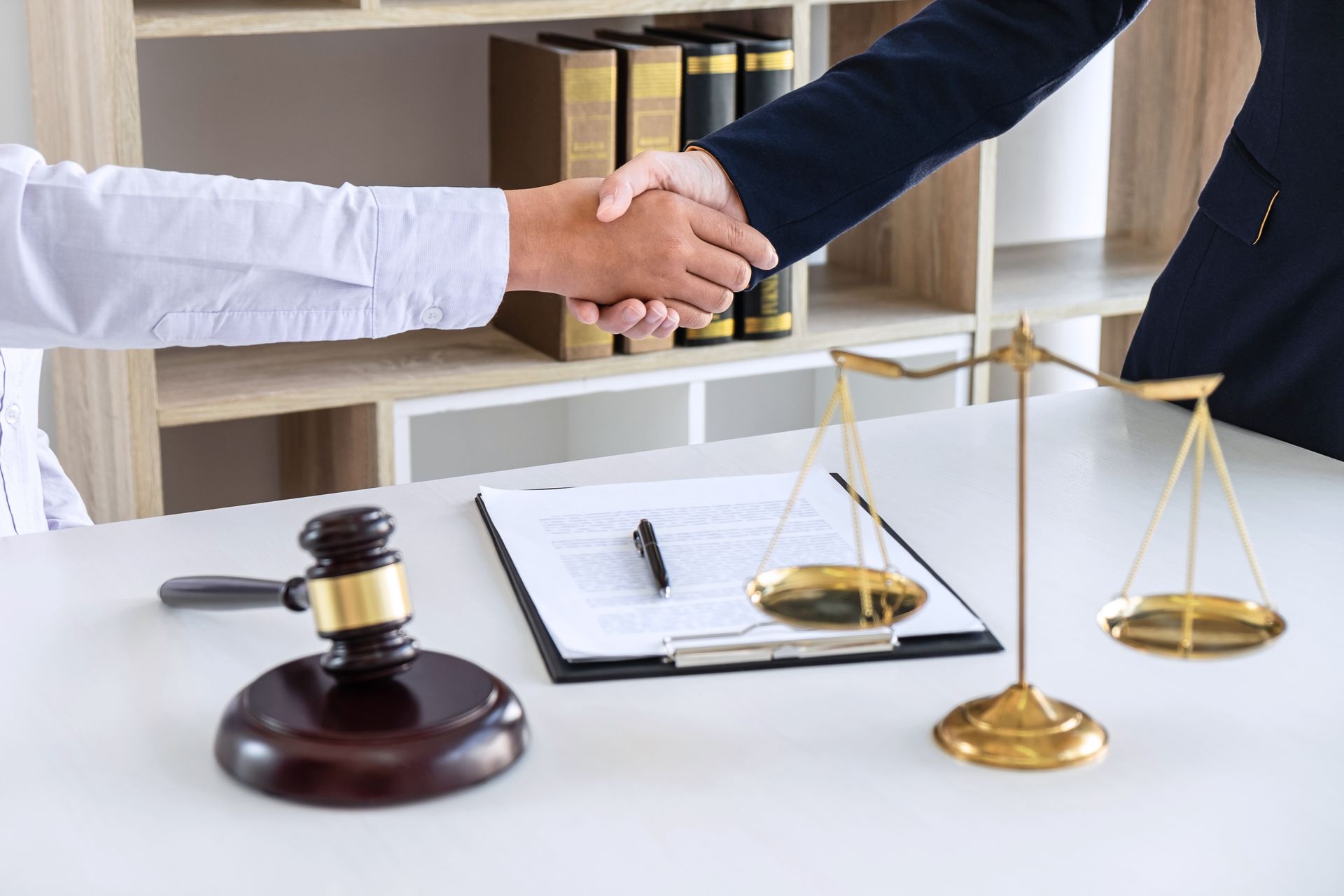 Une poignée de main dans un cabinet d'avocats, avec un marteau, une balance de justice et des documents sur un bureau.