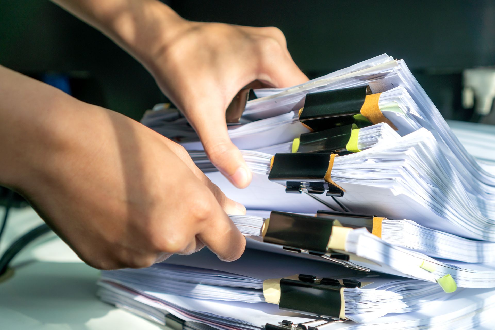 Des mains prennent un dossier dans une épaisse pile de papiers agrafés sur un bureau.
