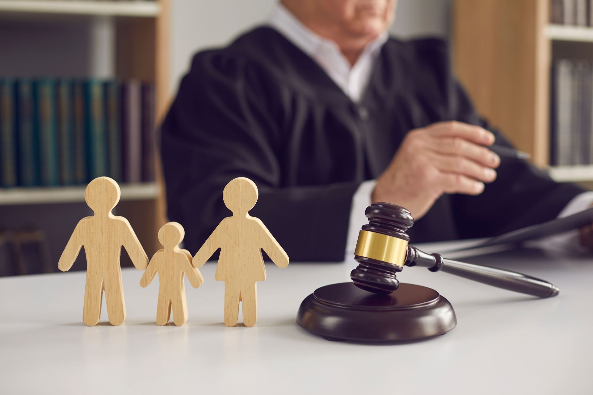 Sur un bureau sont posés une icône d'une famille et un marteau de juge, avec en arrière plan une personne vêtue de noir.