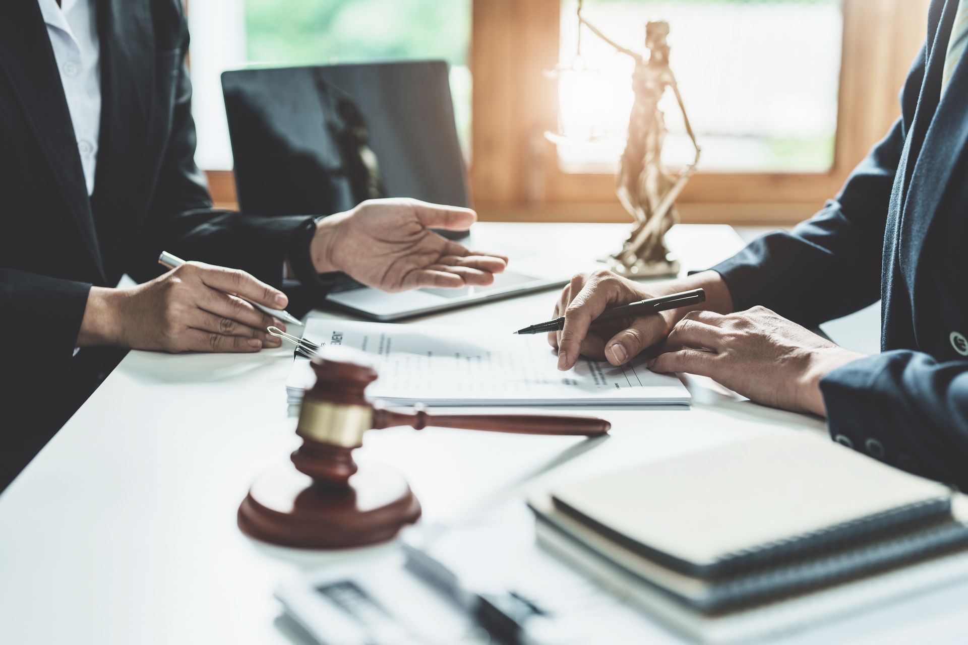 Des avocats en costume autour d'un bureau relisent des documents, avec un marteau et une statue de la justice.
