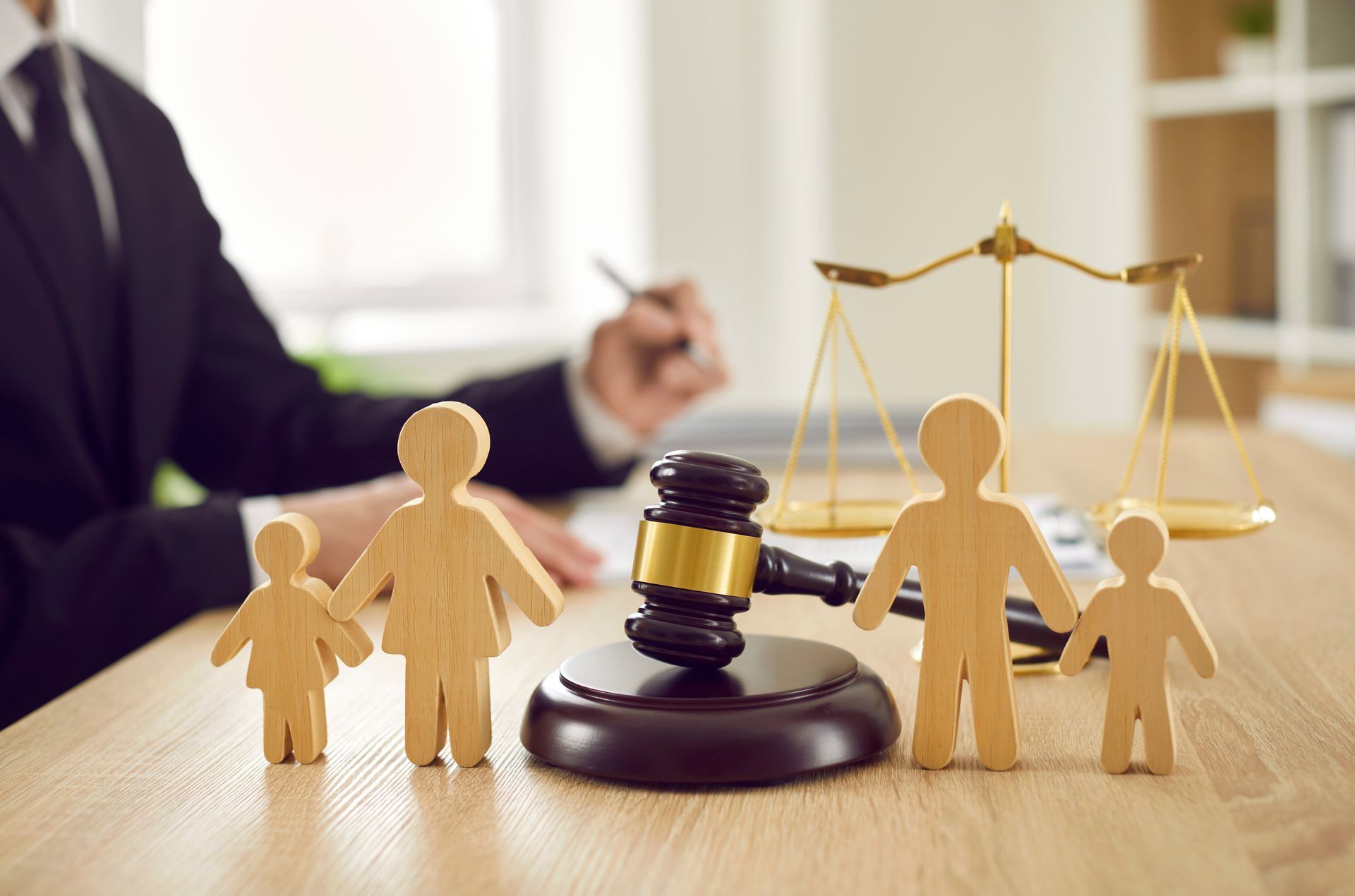 Maillet, balance de la justice et famille en figurines de bois sur un bureau , un avocat est flou en arrière-plan.