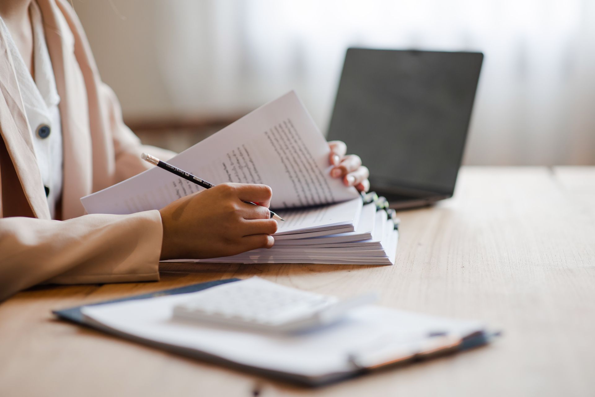 Une personne relit des documents sur un bureau, avec un ordinateur portable en arrière-plan.