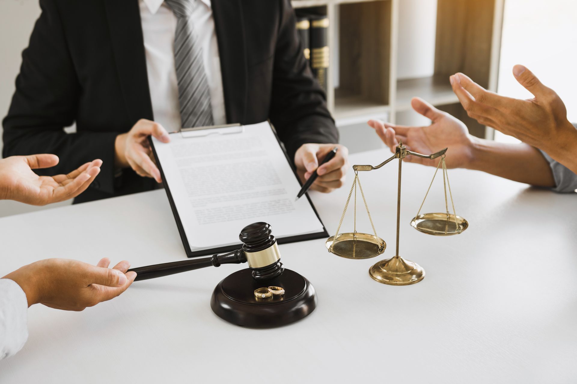 Avocat montrant un document à ses clients autour d'une table où se trouvent un maillet et une balance de justice.
