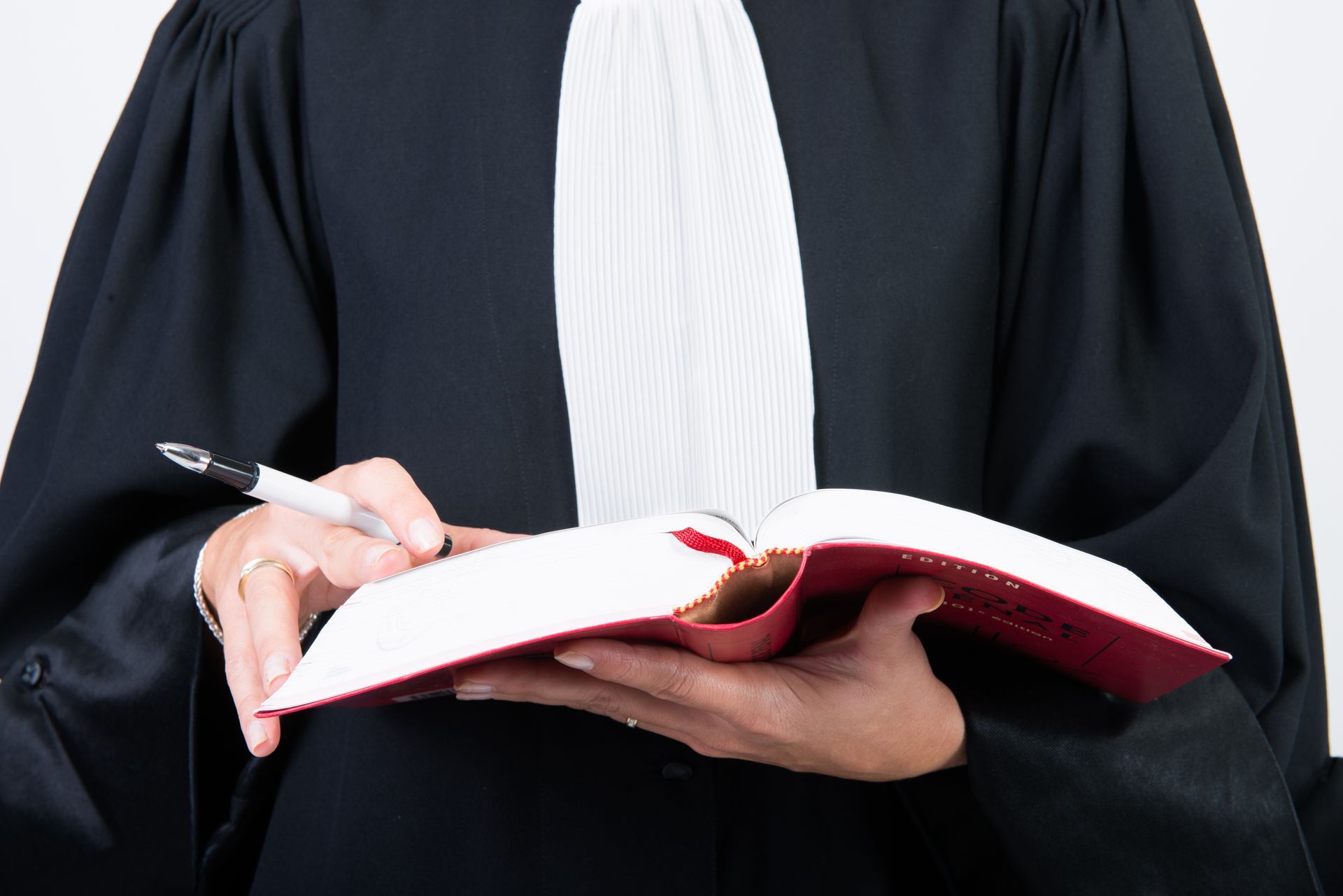 Une personne en robe d'avocat tient un livre ouvert avec un stylo.