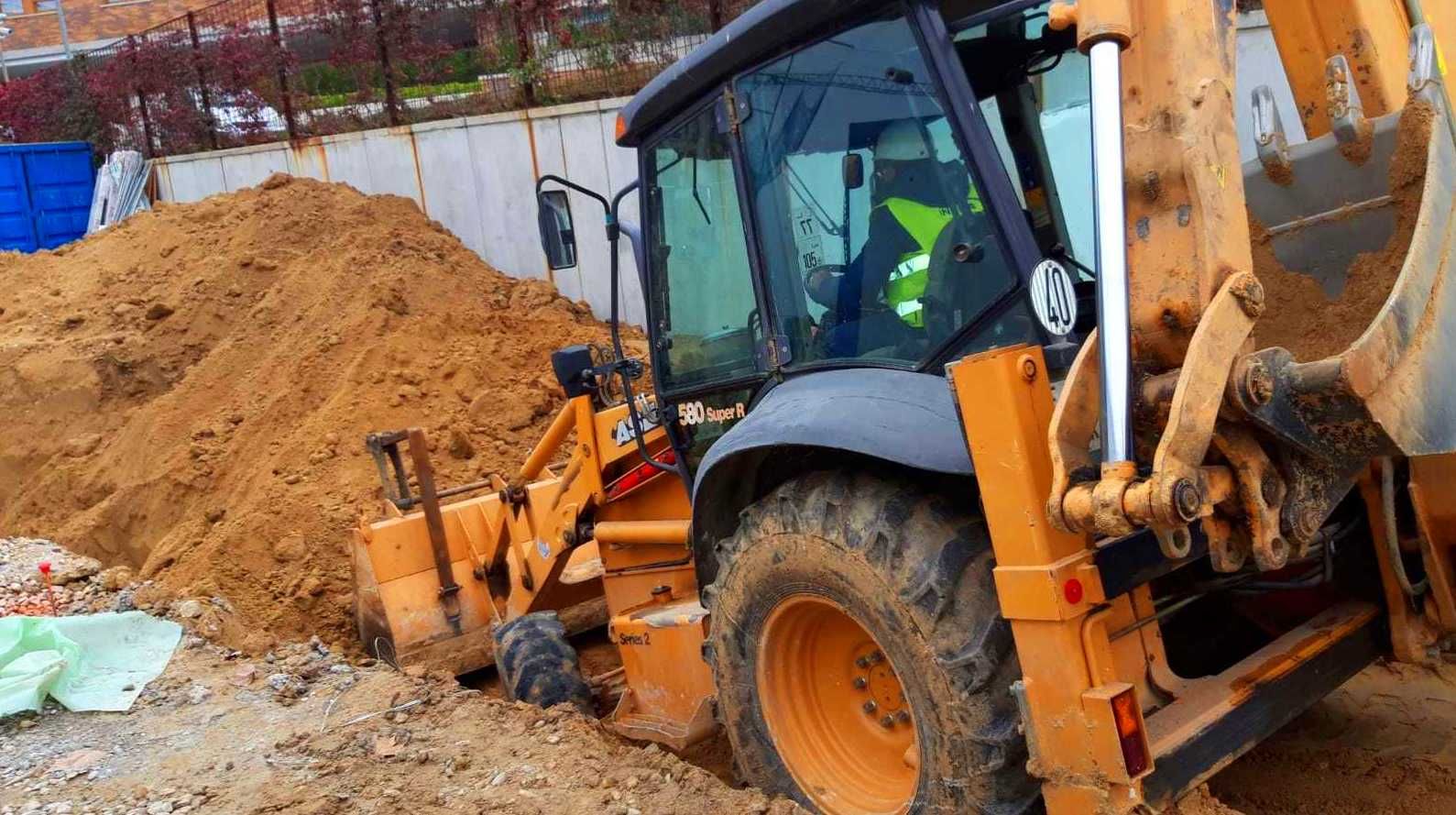 Retroexcavadora excavando en un montón de tierra. Operador visible desde la cabina, en una obra de construcción.