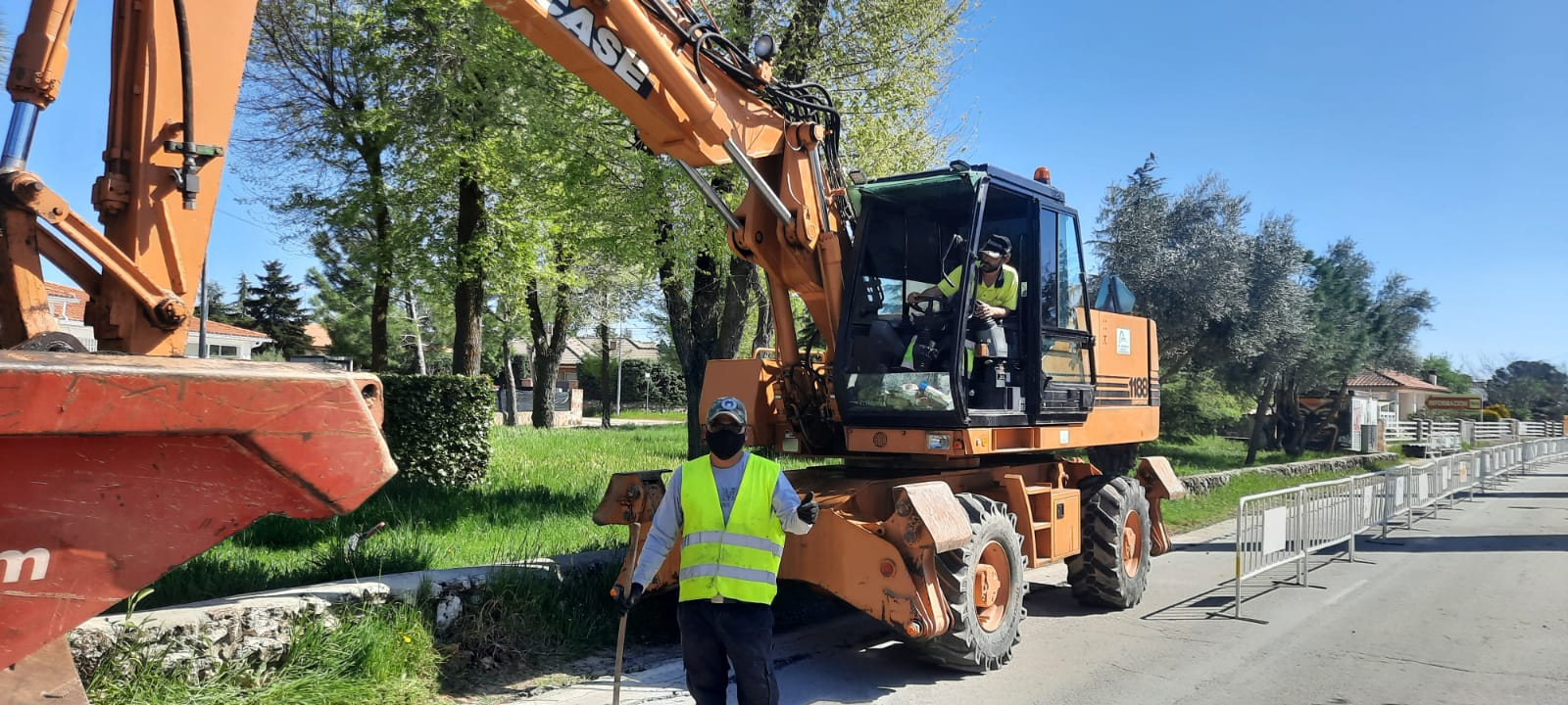 Una excavadora naranja y una persona con chaleco de seguridad trabajando al costado de la carretera.