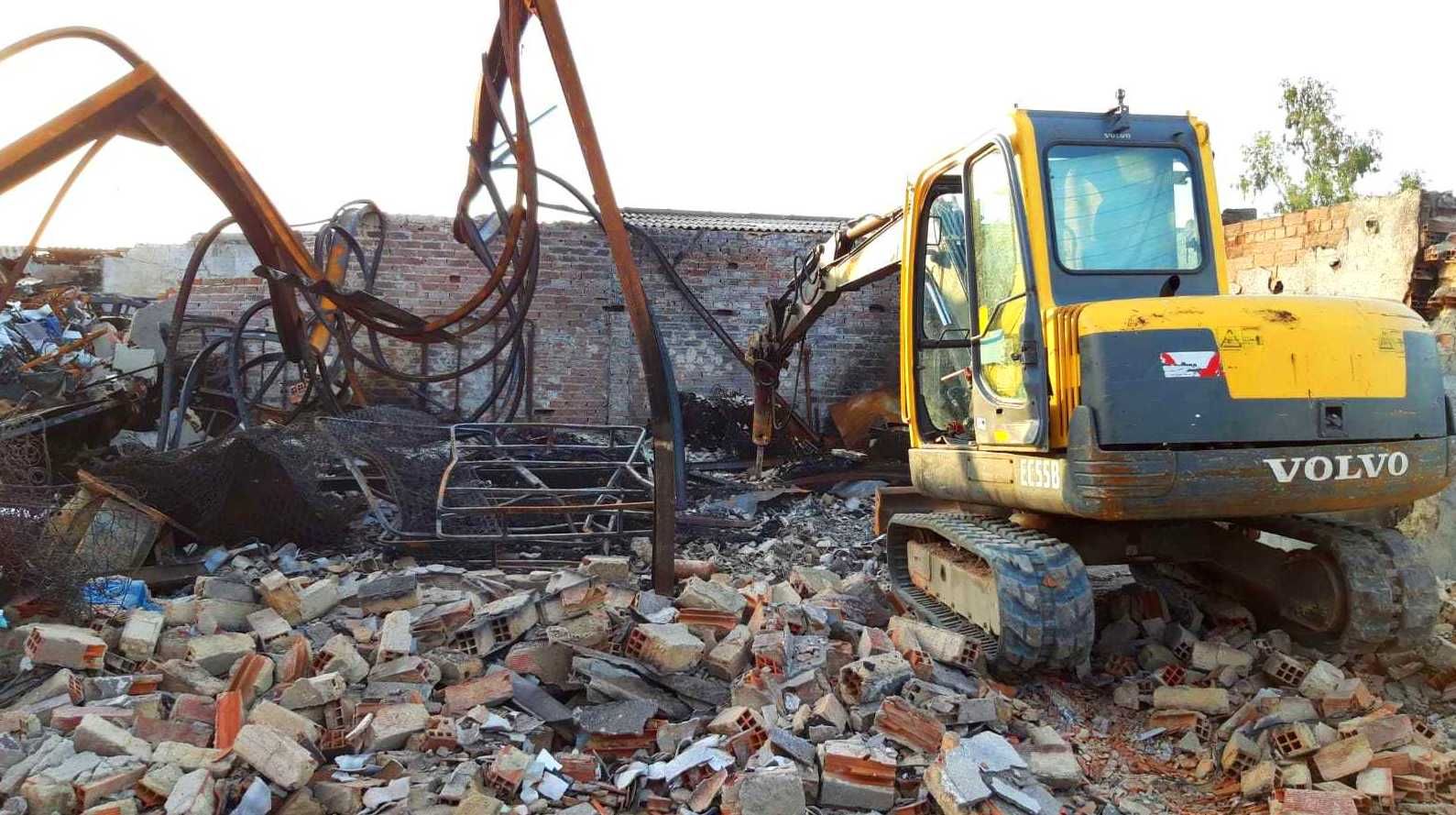 Excavadora Volvo amarilla demoliendo un edificio de ladrillos; los escombros rodean la máquina