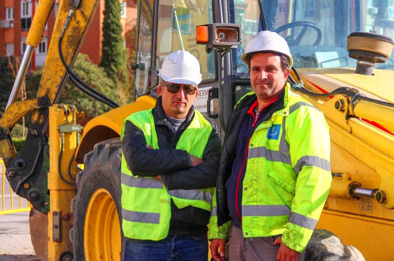 Dos hombres con chalecos de seguridad y cascos de seguridad se encuentran junto a equipos de construcción de color amarillo.