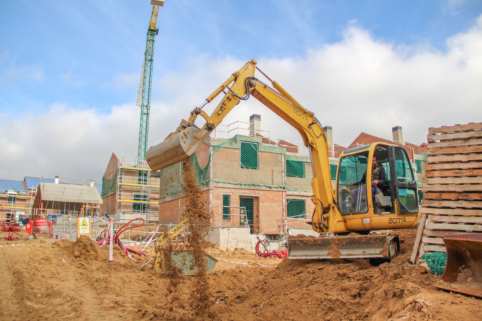 Excavadora amarilla arrojando tierra en un sitio de construcción con edificios parcialmente construidos.