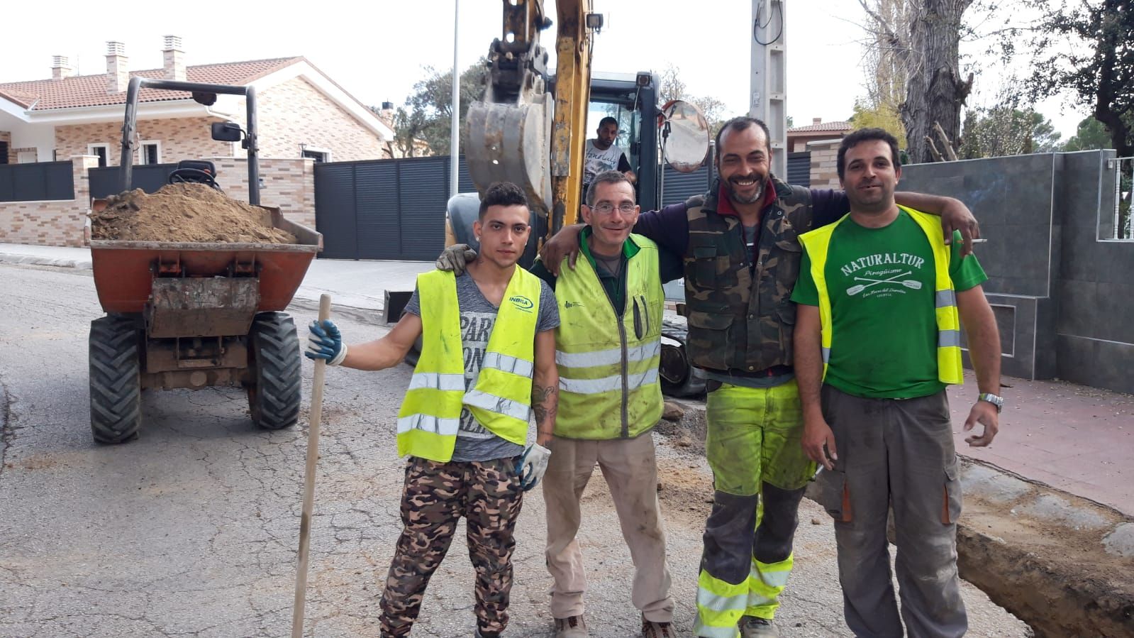 Cuatro trabajadores con chalecos de seguridad posan en una calle con equipos de construcción.