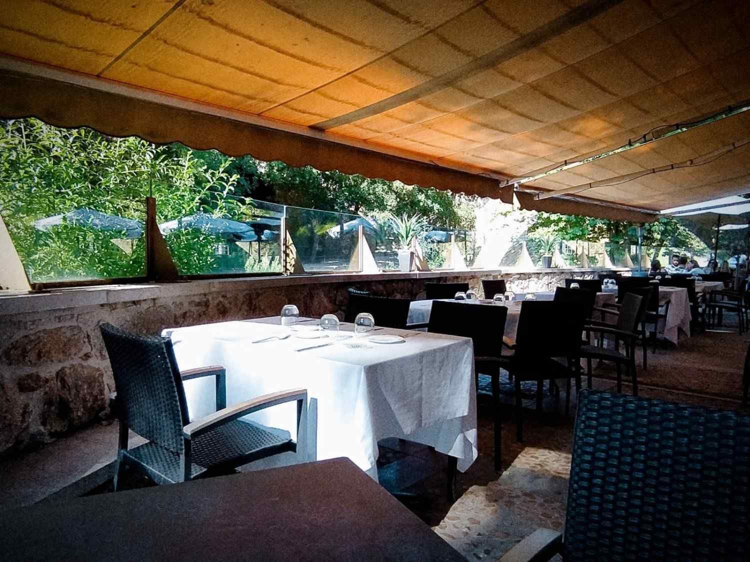 Terraza exterior de un restaurante con mesas cubiertas con manteles blancos bajo un techo que proporciona sombra.
