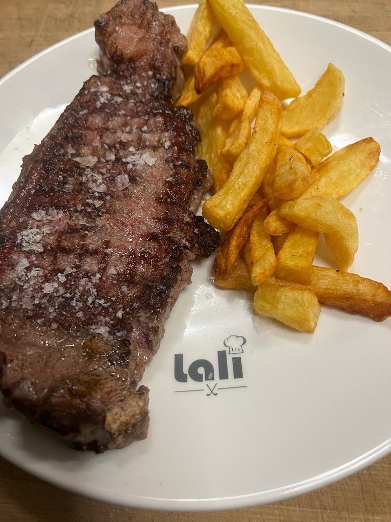 Un filete sellado a la plancha con sal marina gruesa, servido con patatas fritas doradas en un plato con la marca 