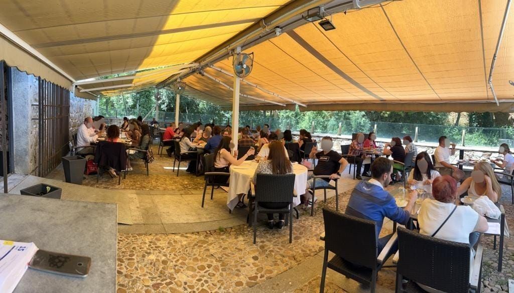 En un día soleado, la gente cena en la concurrida terraza cubierta de un restaurante.