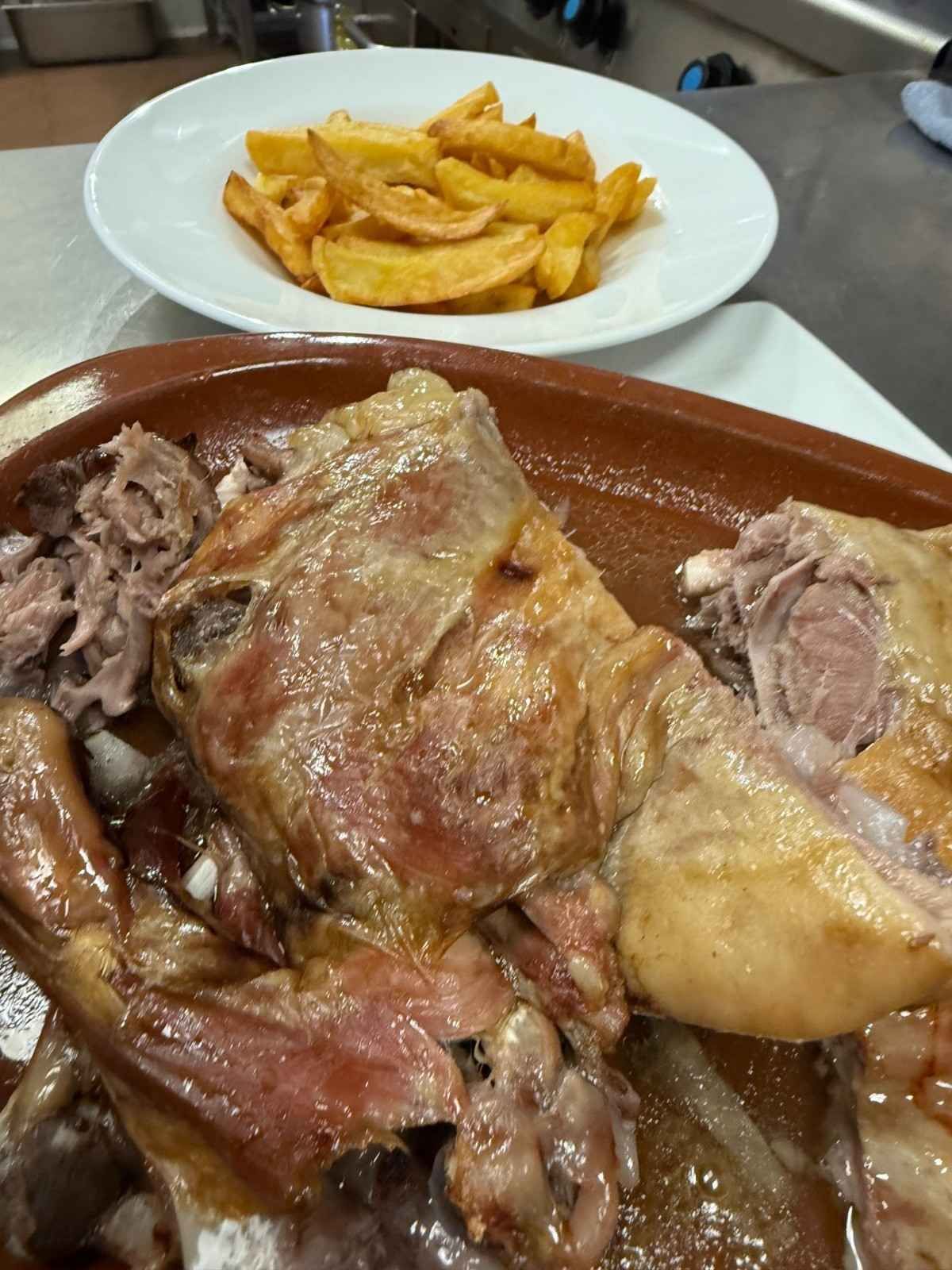 Carne asada servida en un plato de terracota junto a un cuenco blanco lleno de patatas fritas doradas.
