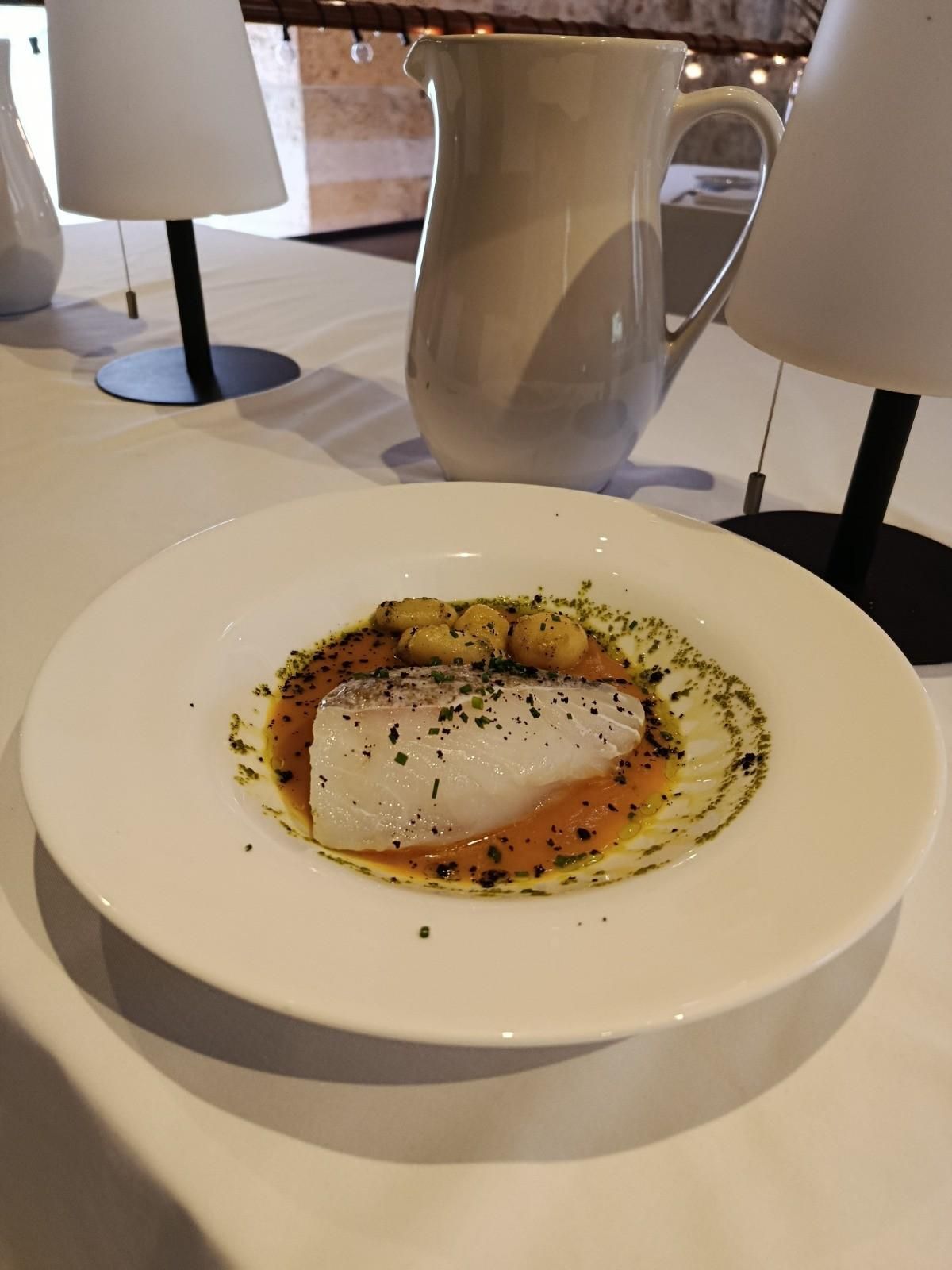 Un cuenco blanco que contiene un filete de pescado blanco en un caldo con pequeños trozos parecidos a patatas.
