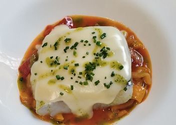 Una porción cuadrada de pescado blanco cubierta con queso fundido y cebollino fresco.