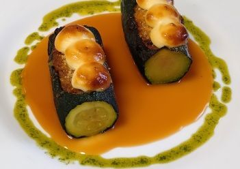 Dos mitades de calabacín cubiertas con trocitos dorados, bañadas en una salsa naranja.