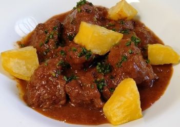 Un plato de estofado de ternera con trozos de carne en una salsa oscura de color marrón rojizo.