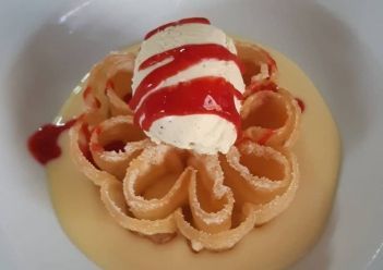 Un pastelito frito con forma de roseta, servido en una base de crema y coronado con una bola de helado .