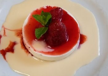 Un postre de panna cotta cubierto con salsa de frambuesa, frutos rojos frescos y menta.