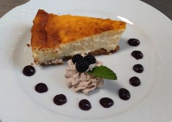 Una porción de tarta de queso adornada con un remolino de mousse, moras frescas, una hoja de menta .