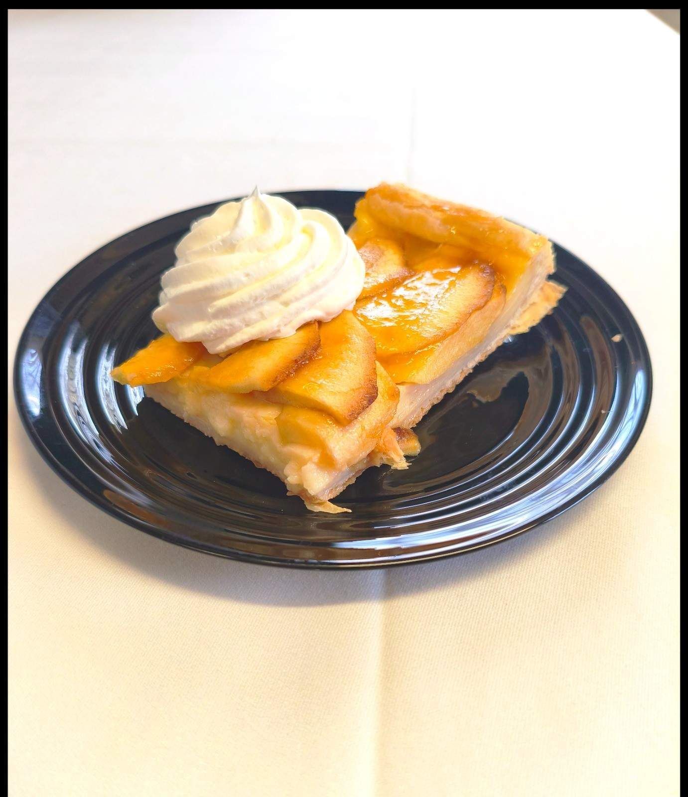 Una porción de tarta de melocotón coronada con una cucharada de nata montada sobre un plato oscuro.