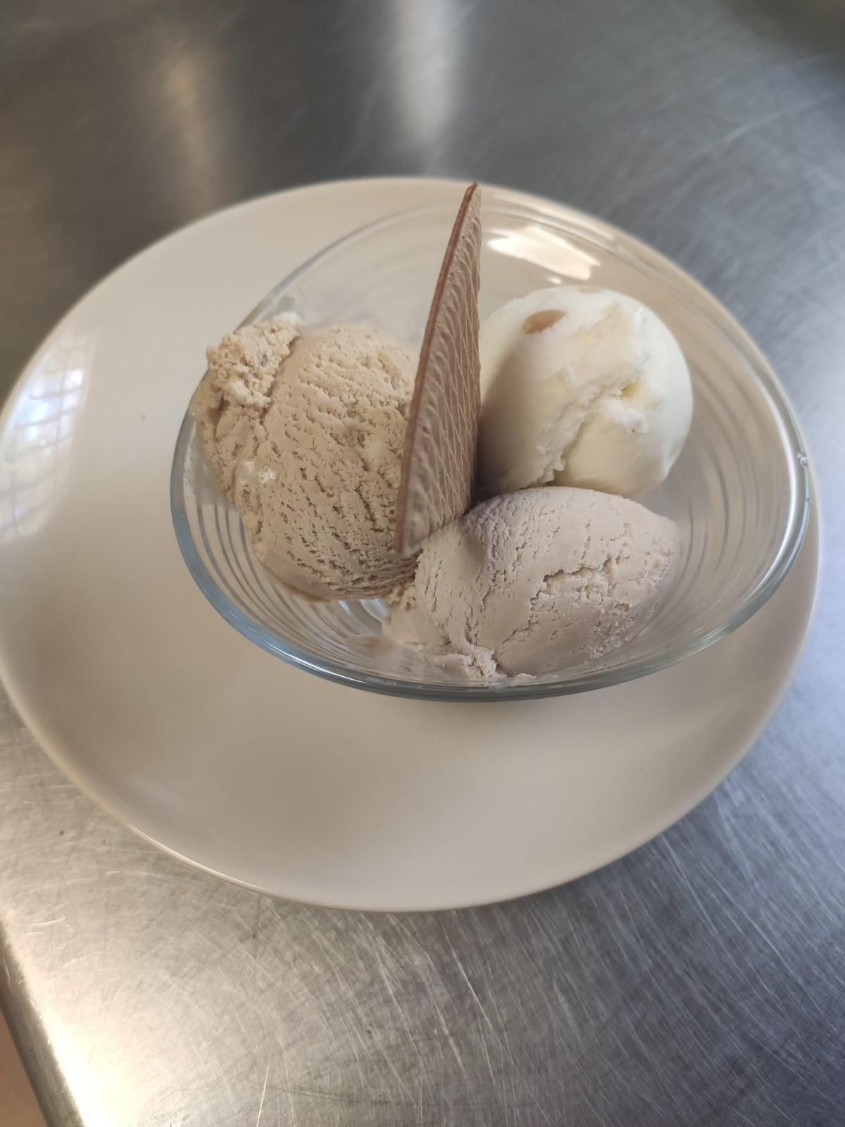 Tres bolas de helado de diferentes colores servidas en un tazón de vidrio con una oblea triangular fina .