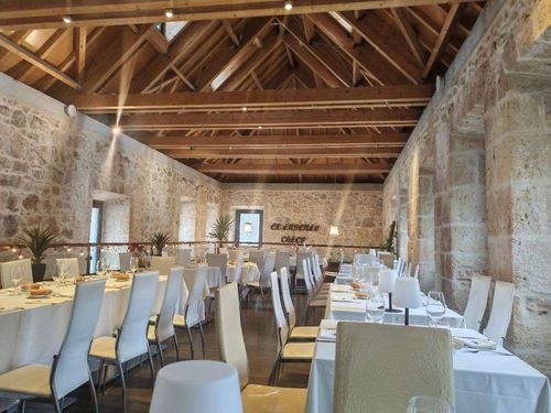 Un salón de banquetes con paredes rústicas de piedra, techos abovedados de madera y mesas dispuestas para un evento .