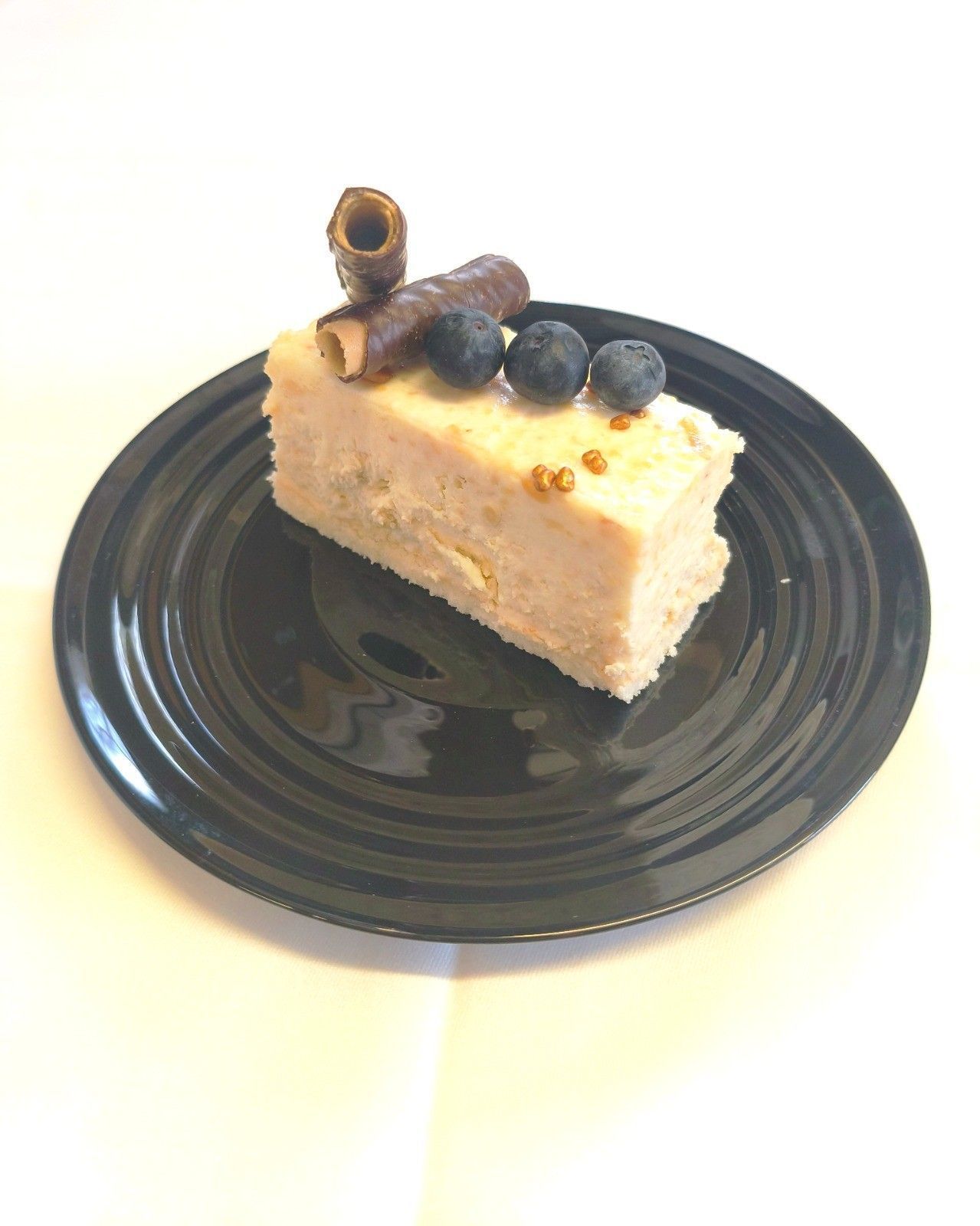 Una porción de pastel de capas con arándanos y obleas de chocolate sobre un plato negro con fondo blanco.