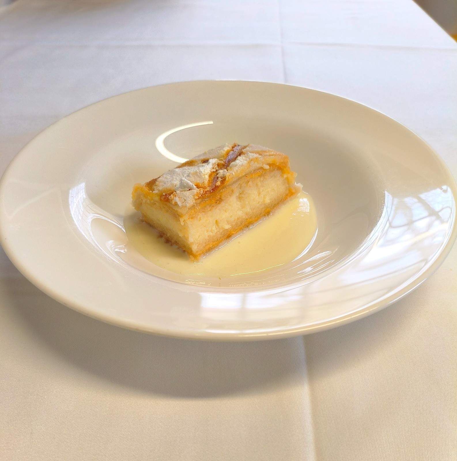 Una sola porción rectangular de pastel cubierta con azúcar glas, servida sobre una base de crema en un plato blanco.