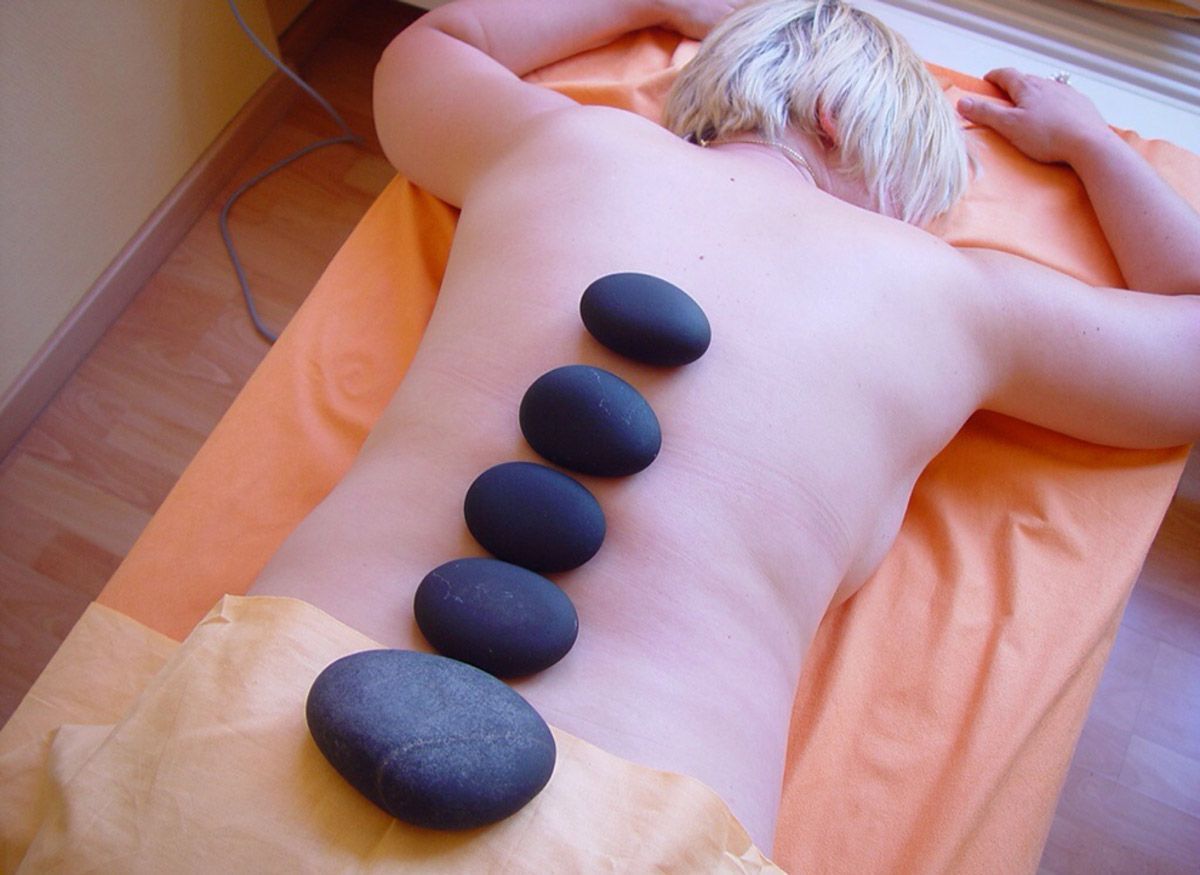 Eine Frau liegt auf der Liege mit warmen Steinen auf dem Rücken