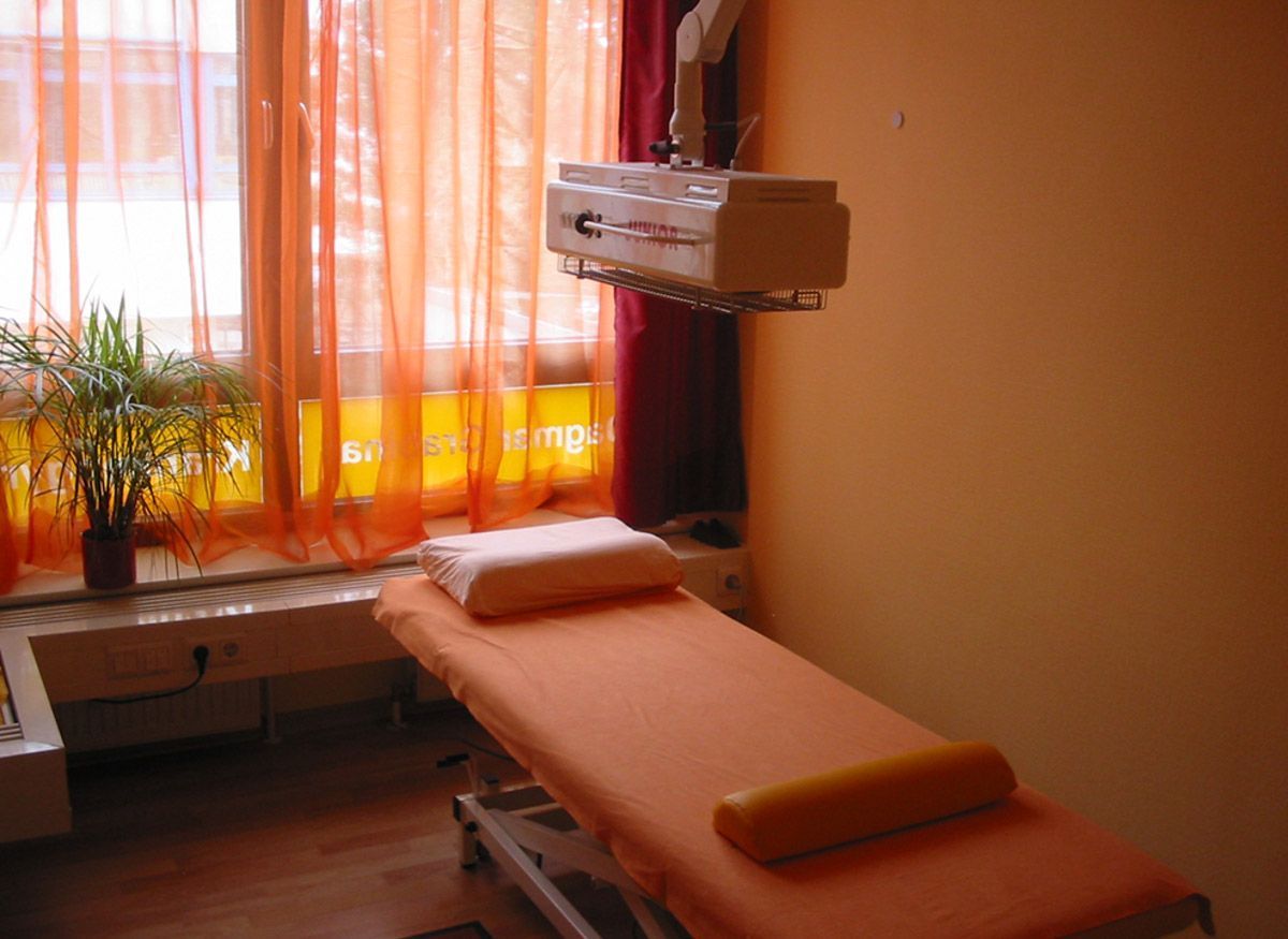 eine Liege steht in einem orangenen Behandlungsraum