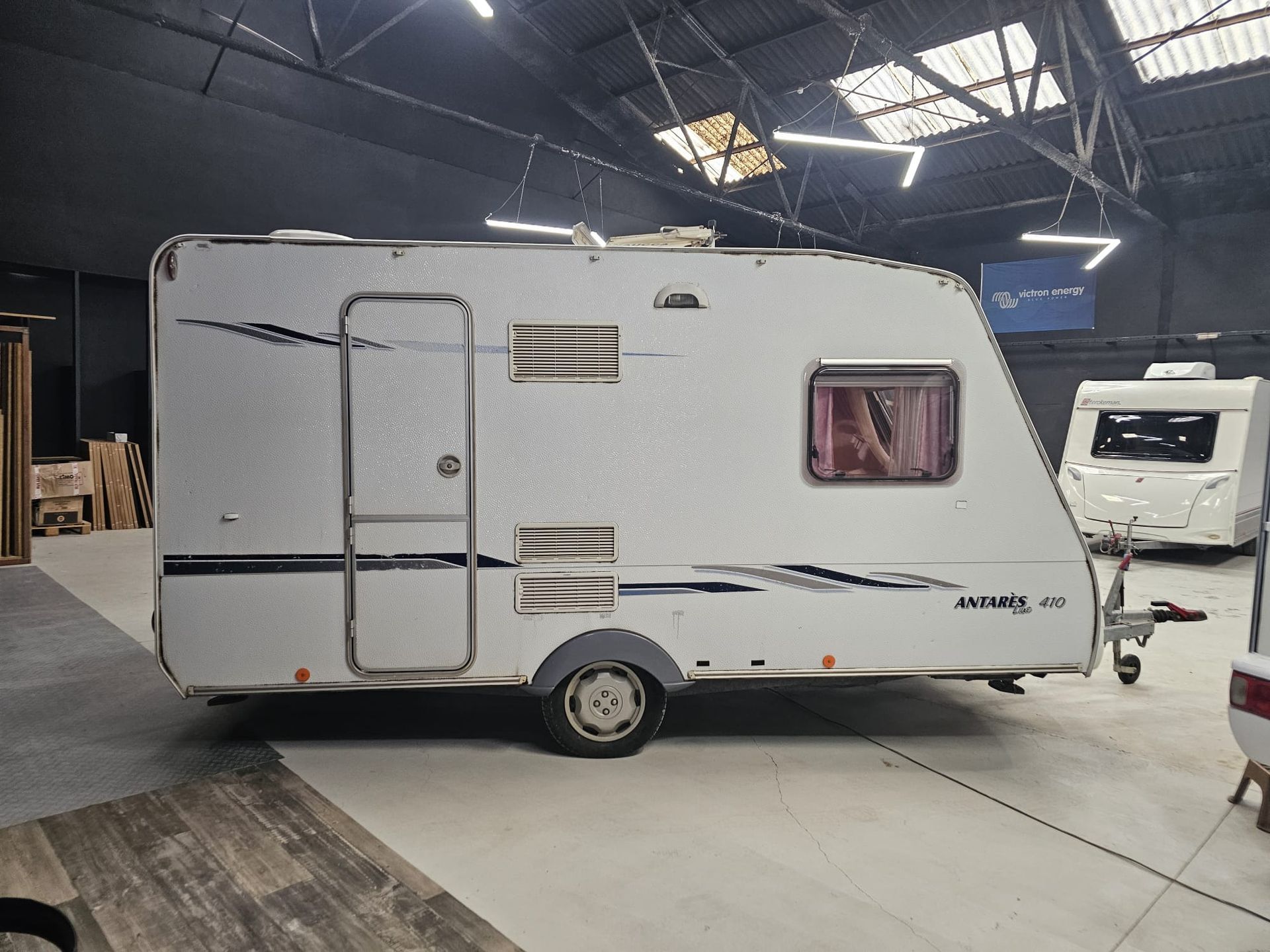 Una caravana blanca está estacionada en un estacionamiento con un cartel que dice compra venta de caravanas