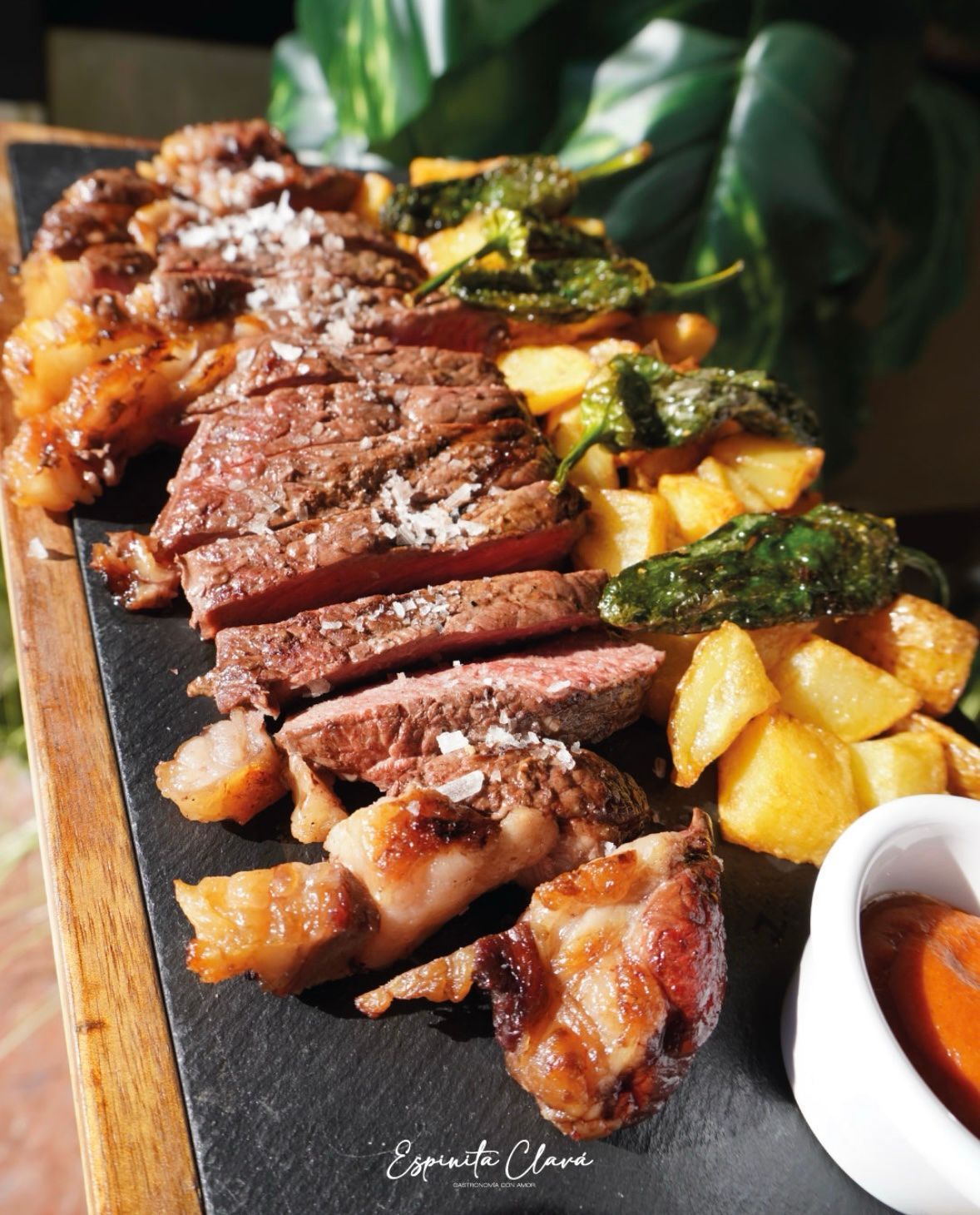 Filete a la parrilla en rodajas con papas fritas y salsa en una tabla de servir negra.