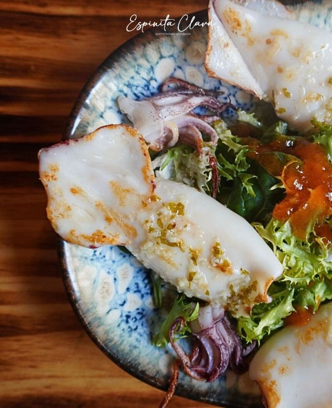 Primer plano de una ensalada de mariscos emplatada con rodajas de calamar, verduras y aderezo de naranja