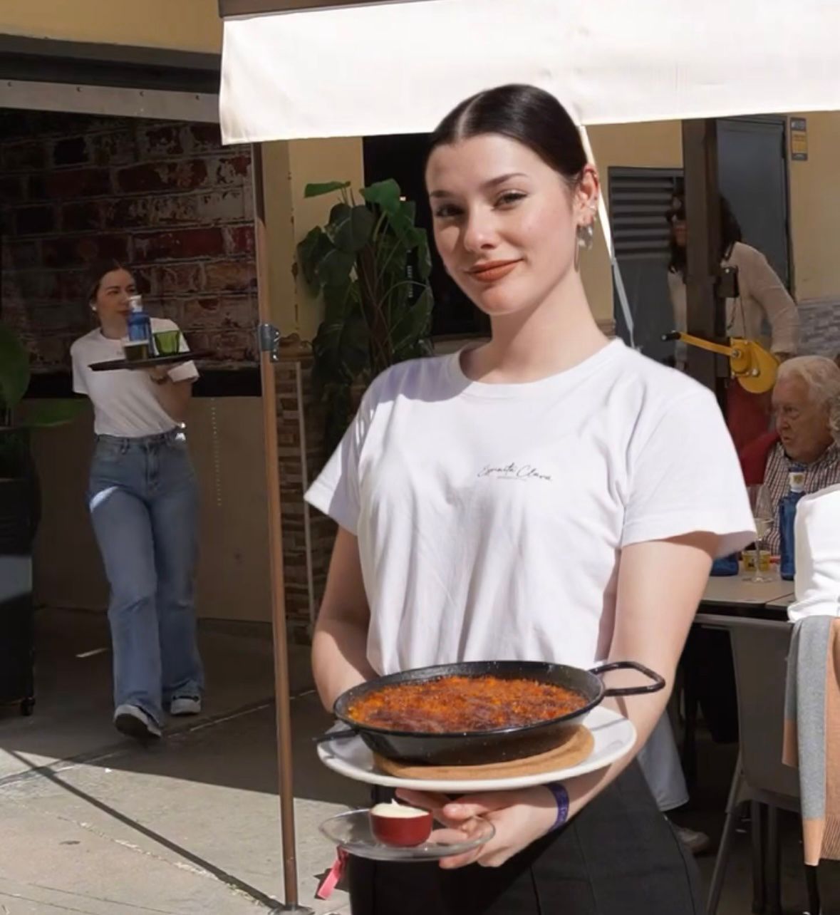 Mujer sosteniendo una pizza en un evento al aire libre bajo una carpa.