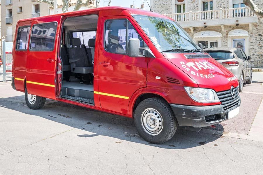 Camionnette de taxi rouge, porte ouverte, stationnée sur une aire pavée près du bâtiment.