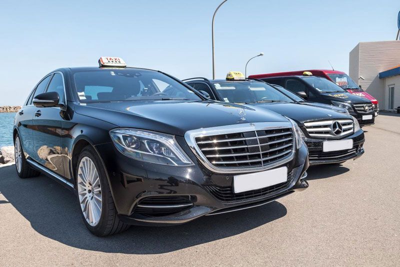 Des taxis Mercedes-Benz noirs garés en rang, avec la mer visible en arrière-plan par une journée ensoleillée.