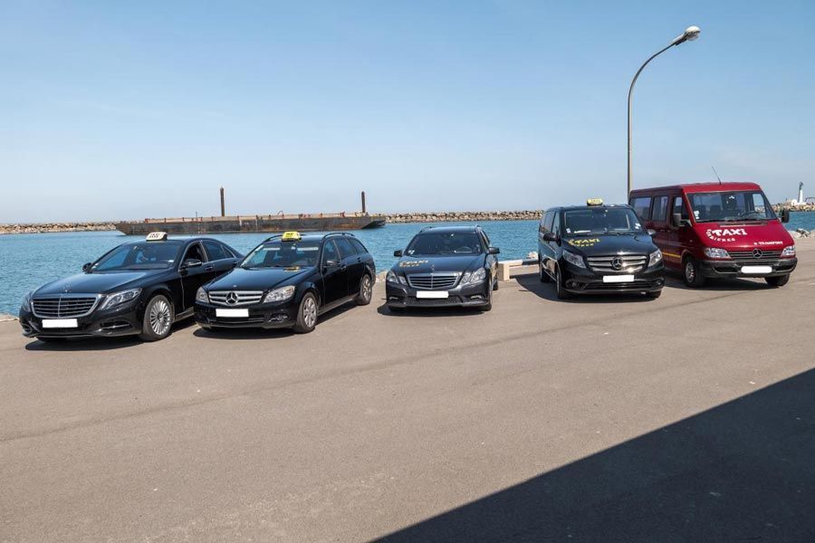 Plusieurs taxis noirs et une camionnette rouge étaient garés le long du front de mer par une journée ensoleillée.