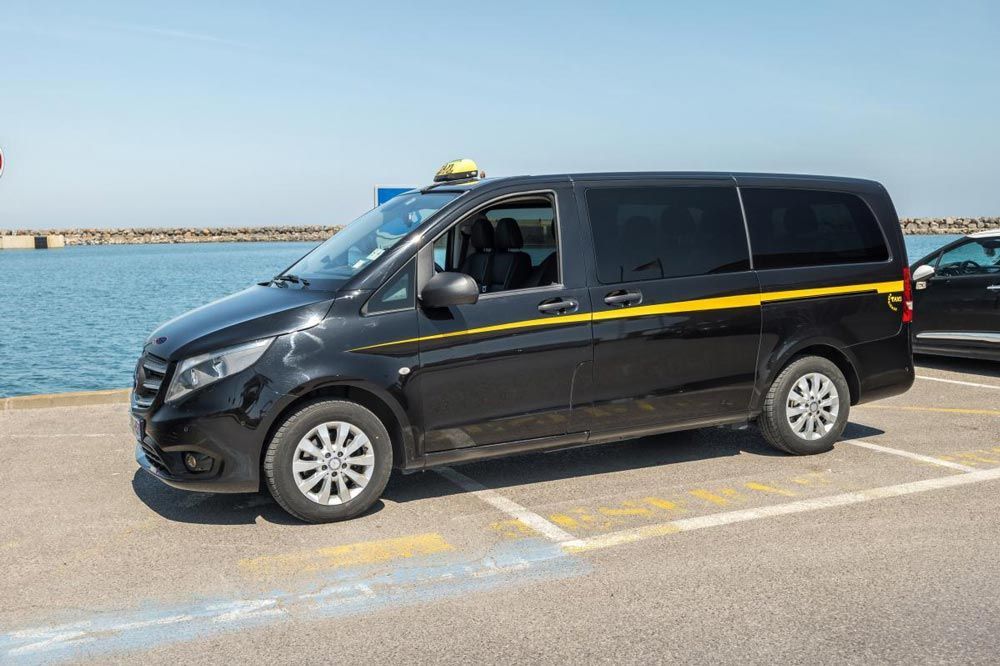 Un taxi-fourgonnette noir est stationné près de l'eau avec une bande jaune sur le côté.