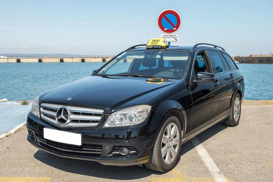 Taxi Mercedes noir stationné au bord de l'eau, avec un panneau « stationnement interdit » visible.